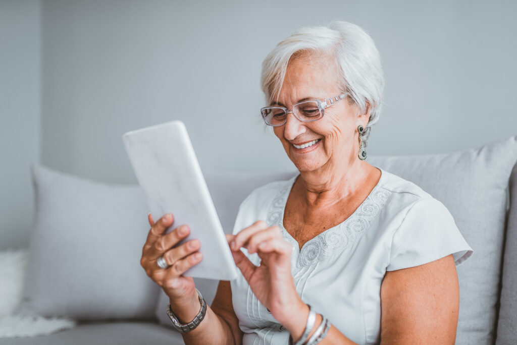 Senior elderly woman using electronic tablet at home. Middle-aged woman reading a message, e-book or information on her tablet computer with a look of excited anticipation as she sits on a couch at home