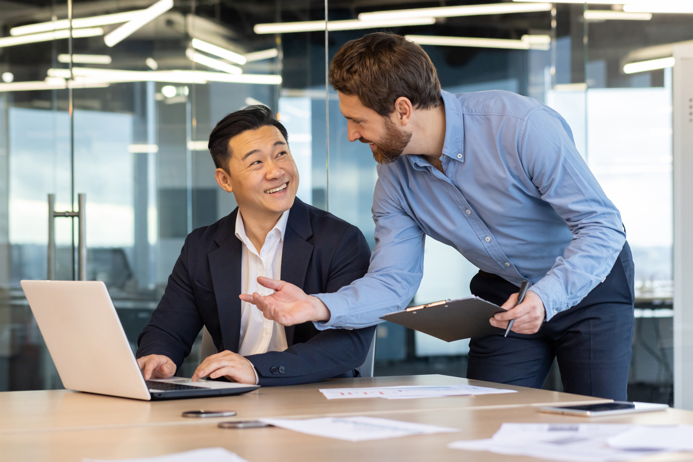 Two multicultural businessmen in suits discussing work over a laptop.