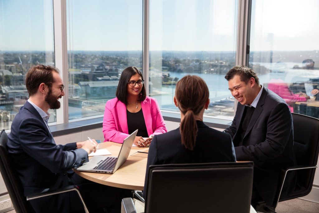 Three professionals in business attire discussing at a conference table in a modern office setting.