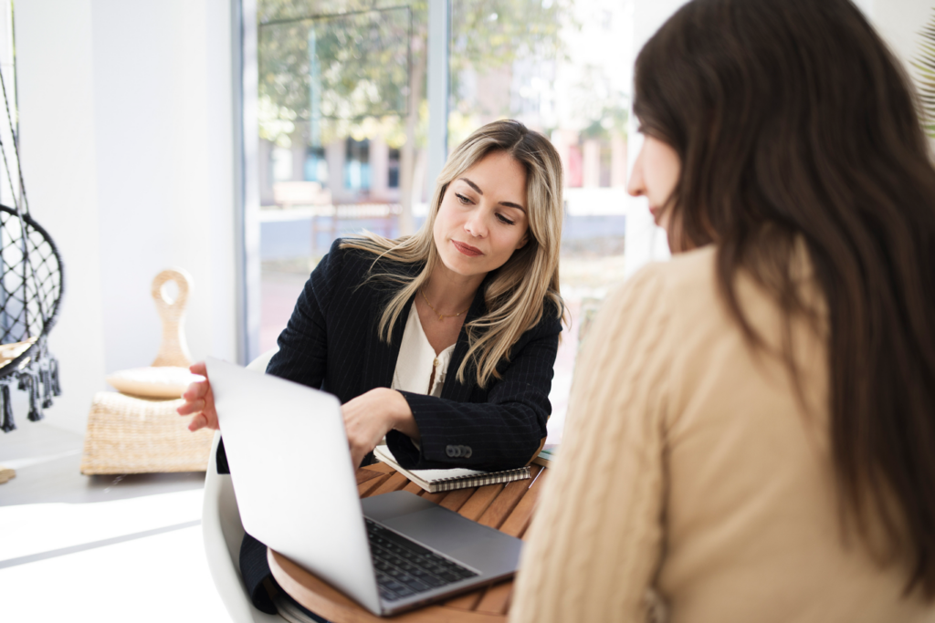 Two women working together at a table with a laptop, sharing ideas.