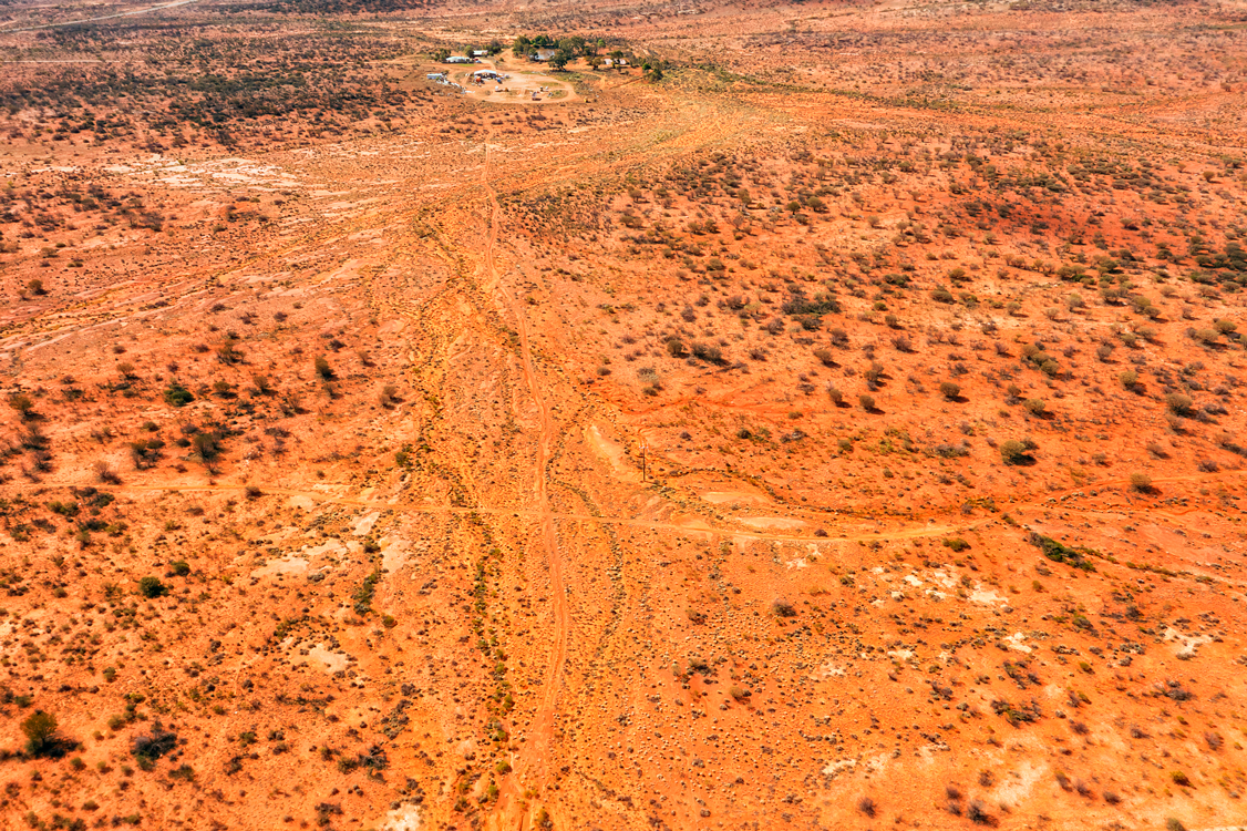 Aerial view of Australian dessert landscape with winding road cutting through red sandy terrain.