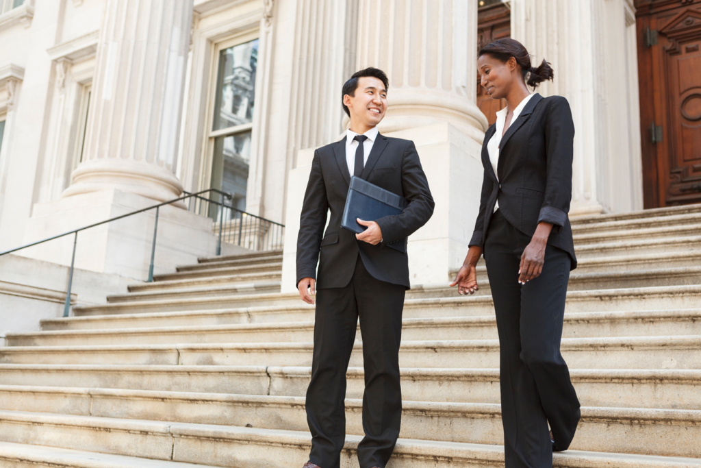 Businessman and businesswoman in formal attire descending steps at court house.