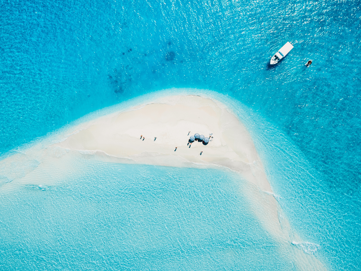 Aerial view of a small island with a boat in the water, surrounded by clear blue ocean on a sunny day.