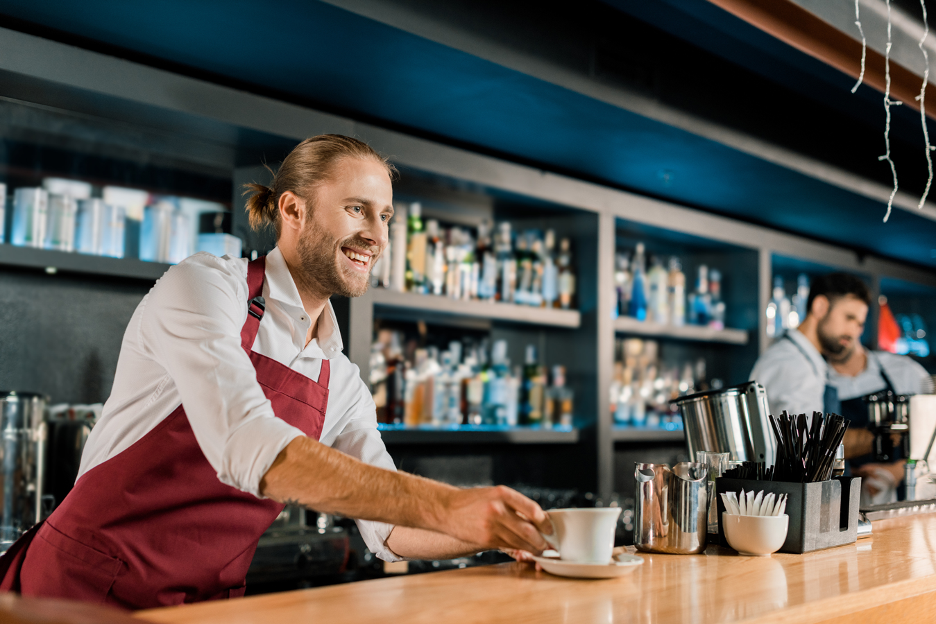 A man in an apron standing behind a bar, preparing drinks.