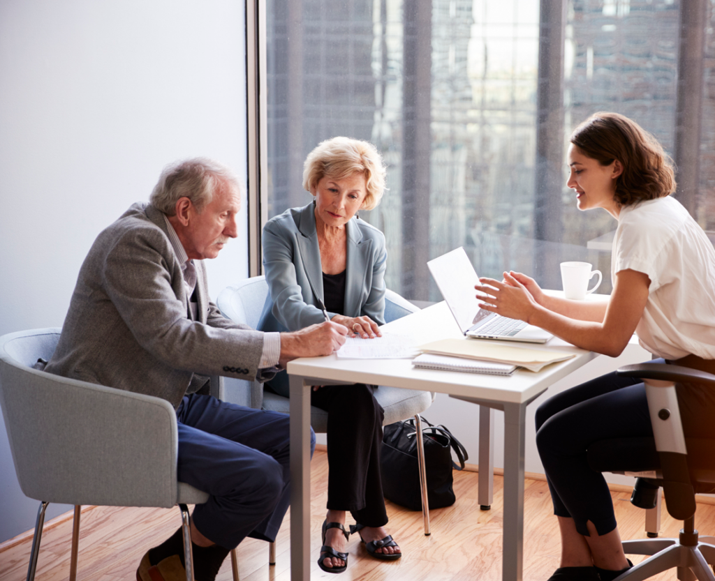 Senior Couple Signing Document In Meeting With Female Financial Advisor In Office