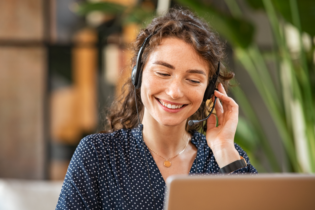 A smiling woman wearing a headset while using a laptop.