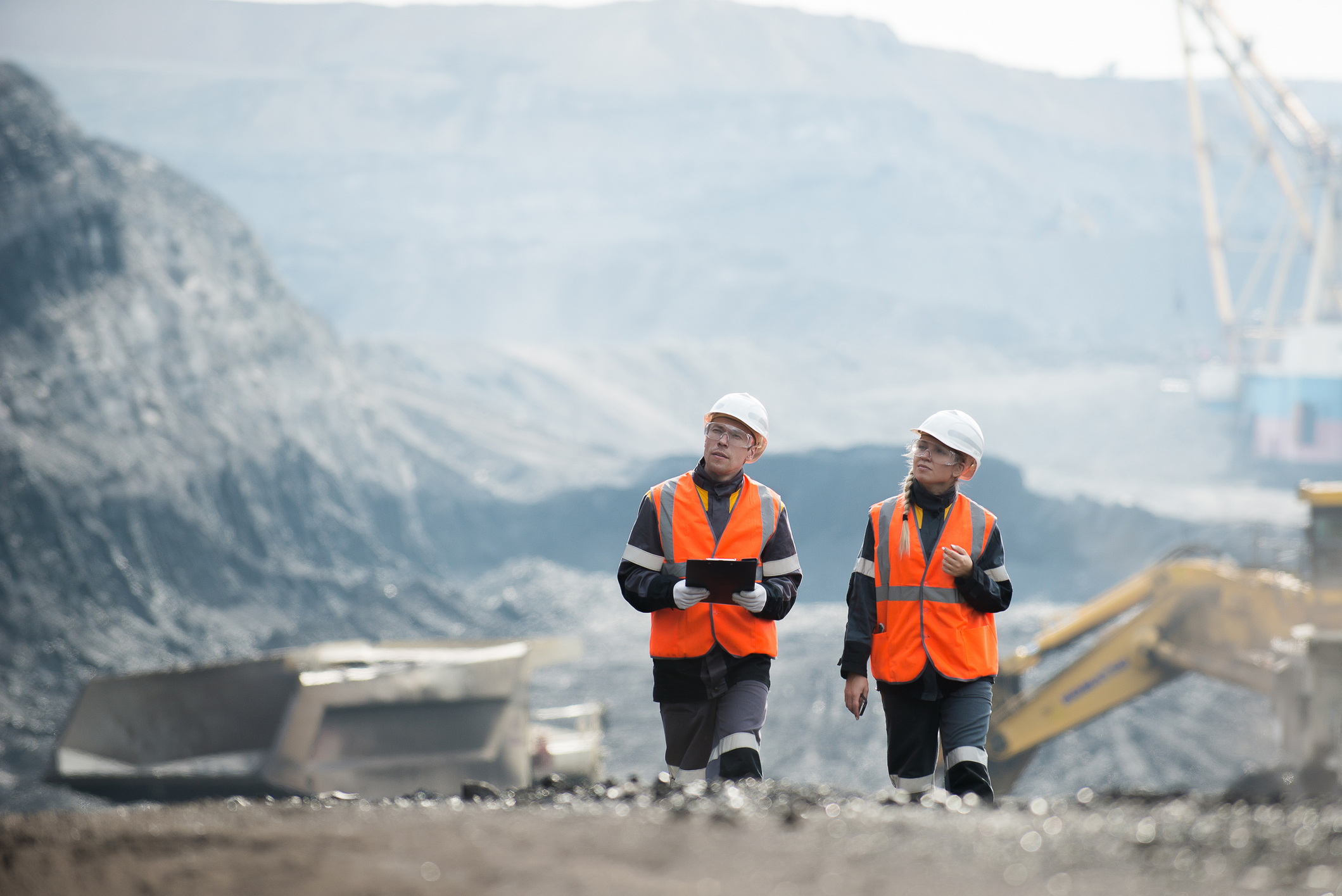 Two workers in hard hats and vests standing in front of a coal mine entrance.