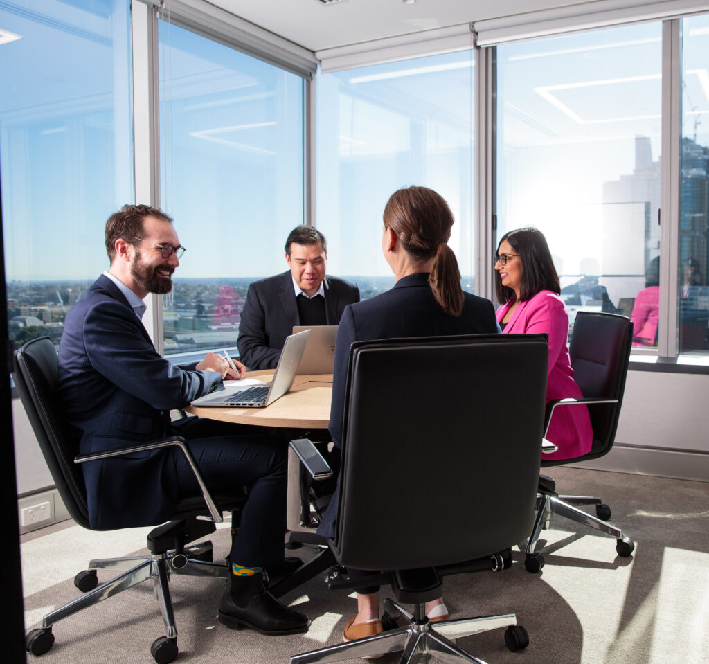 four people in meeting room at round table working and smiling