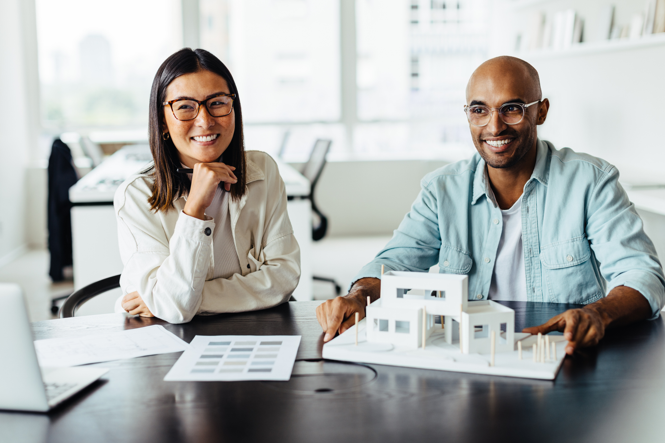 Two young architects working with a 3D house model in an office. Happy business people planning a building project in a design office.