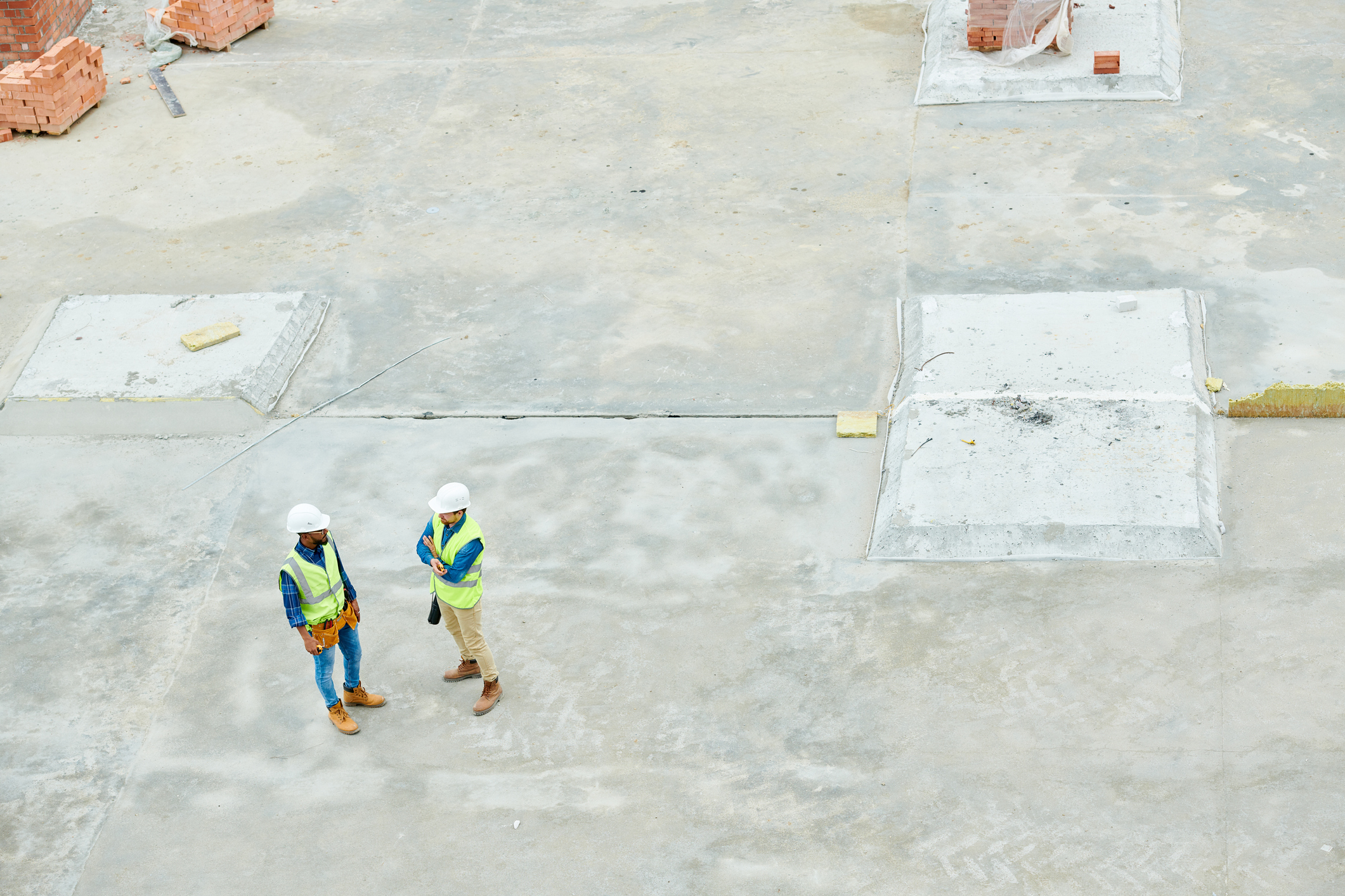 Top view portrait of two workers standing on concrete floor of construction site and discussing project, copy space background.