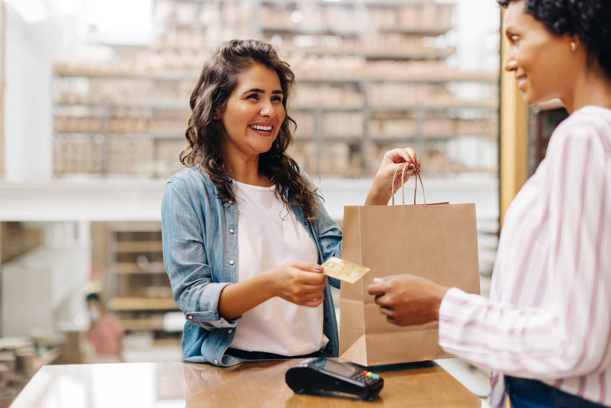 Happy female customer paying her bill with a credit card in a ceramic store. Cheerful young woman smiling happily while shopping from a local female-owned small business.