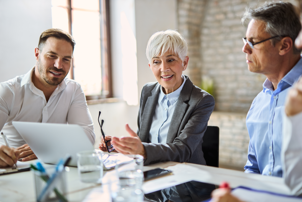 Three professionals discussing work at a table with a laptop.