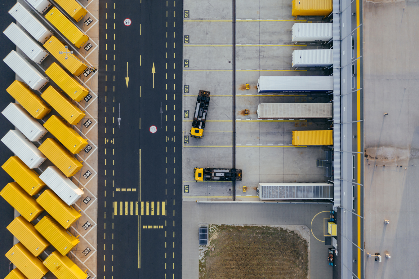 An aerial view of a large warehouse with yellow trucks parked outside.