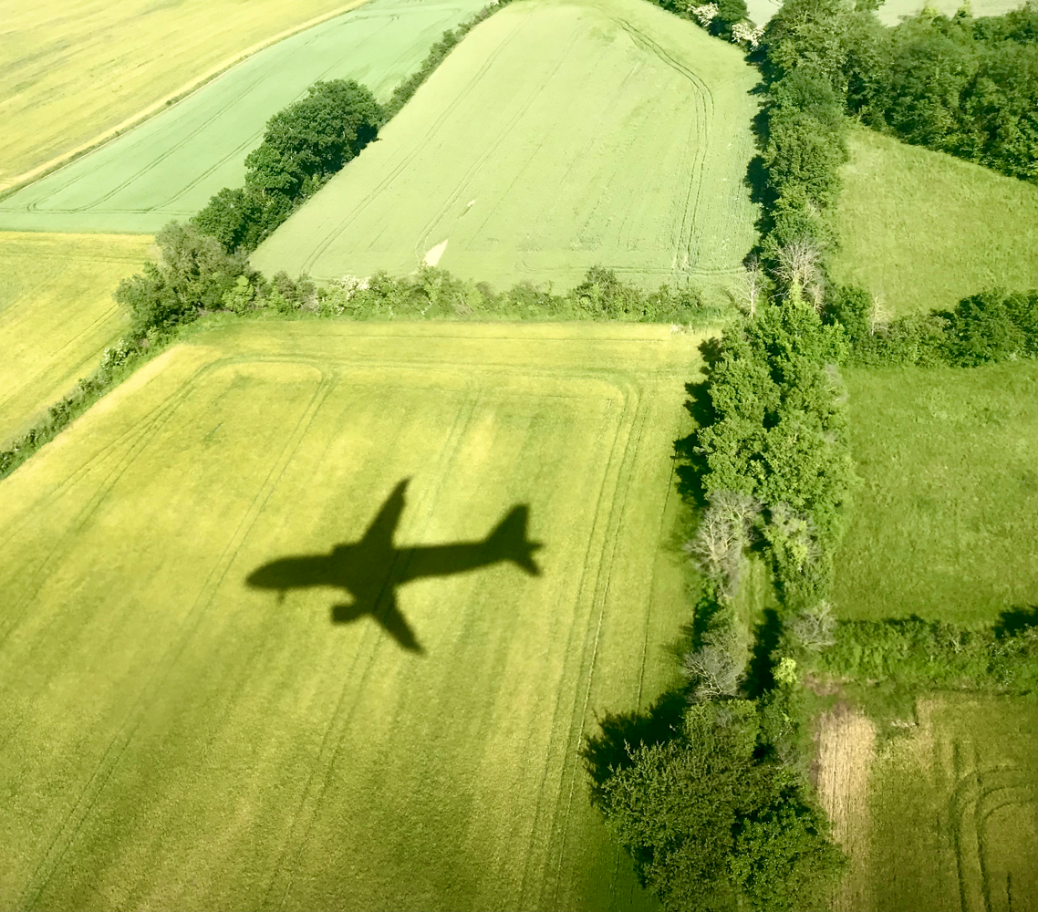 An airplane shadow on a field, showcasing the aircraft's silhouette against the grassy landscape below.