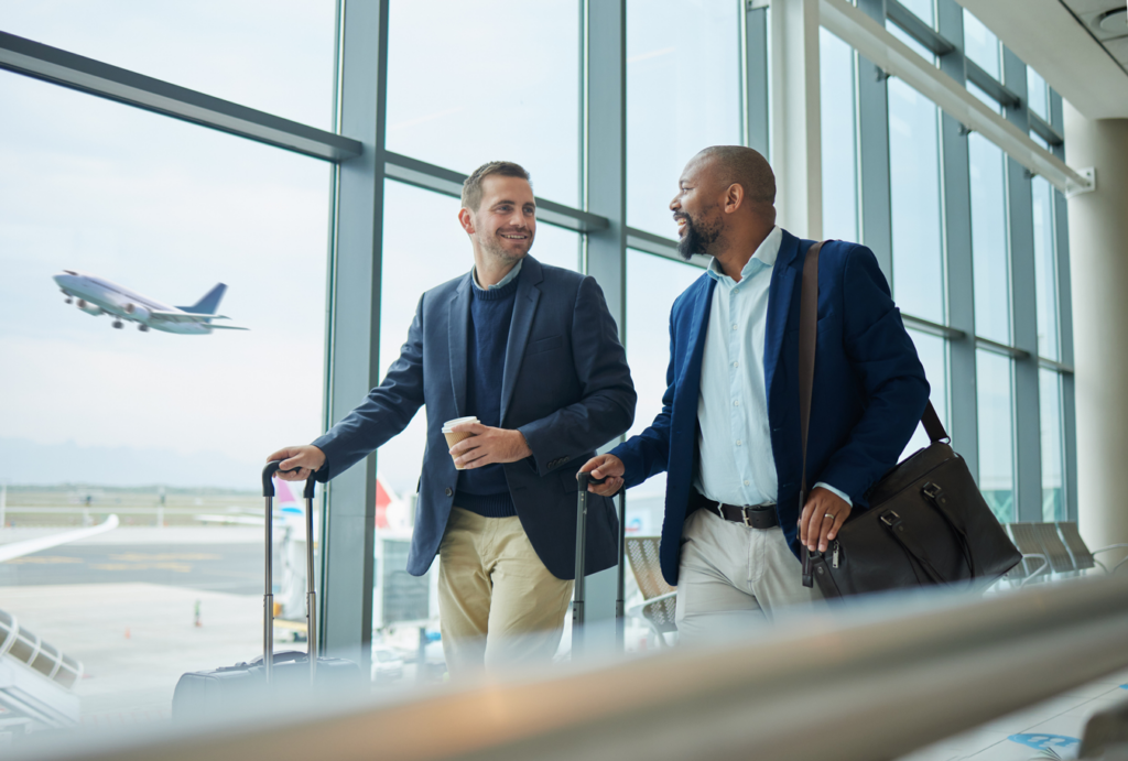 Two business men walking through airport with luggage and coffee