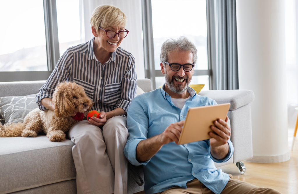 Older couple and dog, looking at tablet in home living room