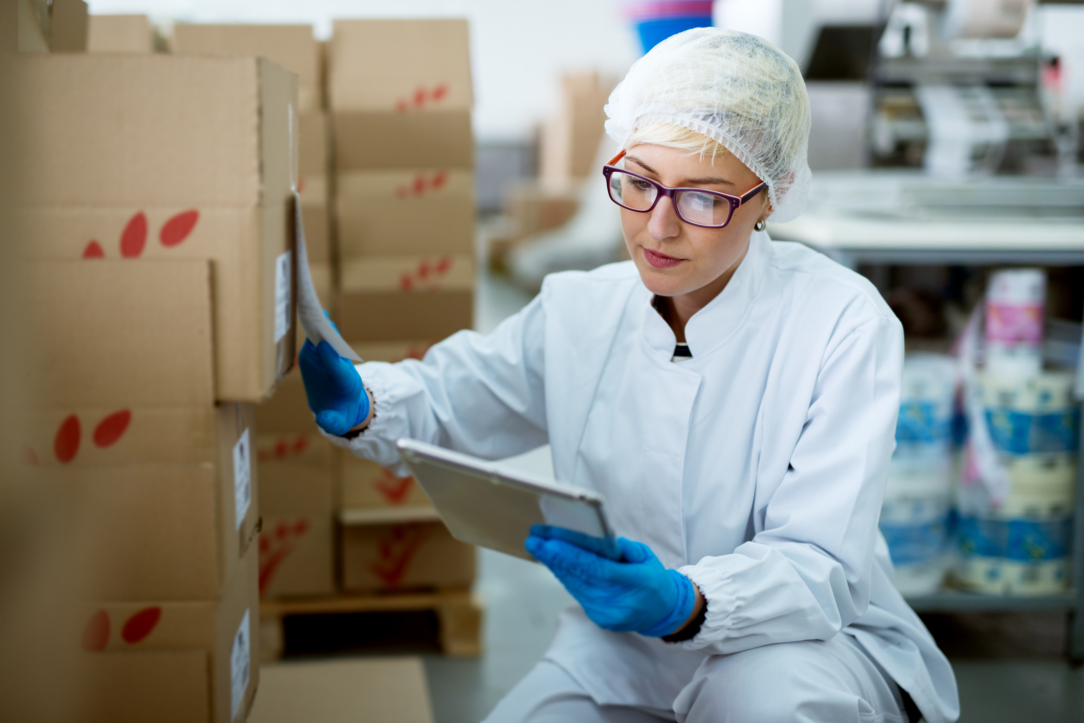 Young focused female worker in sterile cloths using a tablet to check correction of inventory in factory storage room.