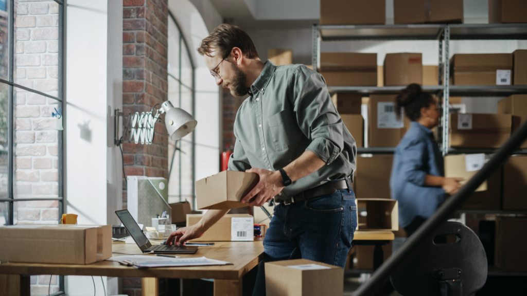 Small business owners Working on laptop whilst also preparing and packing parcels for delivery