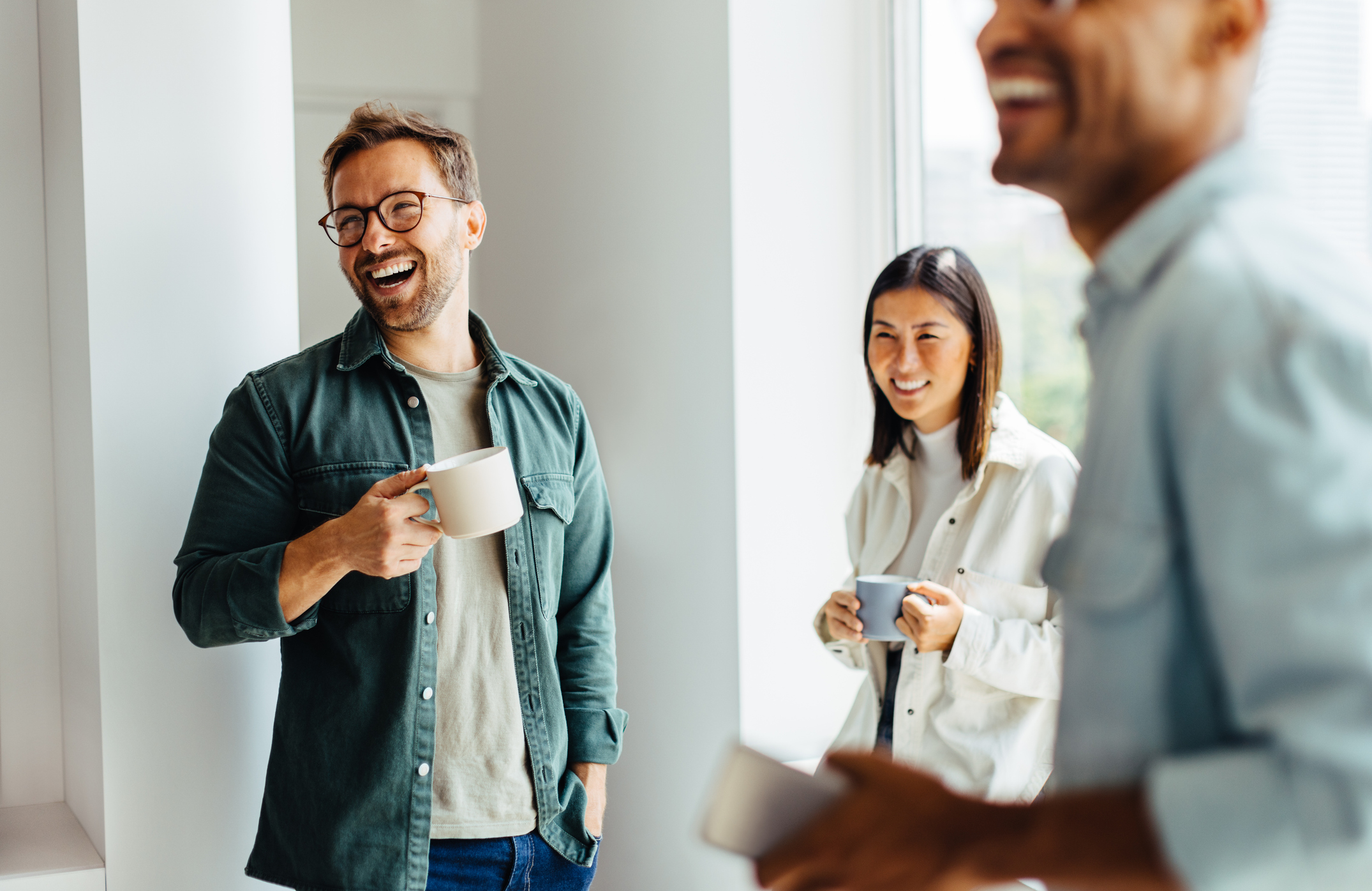 Business people laughing together during a coffee break at work. Group of young professionals standing together in an office.