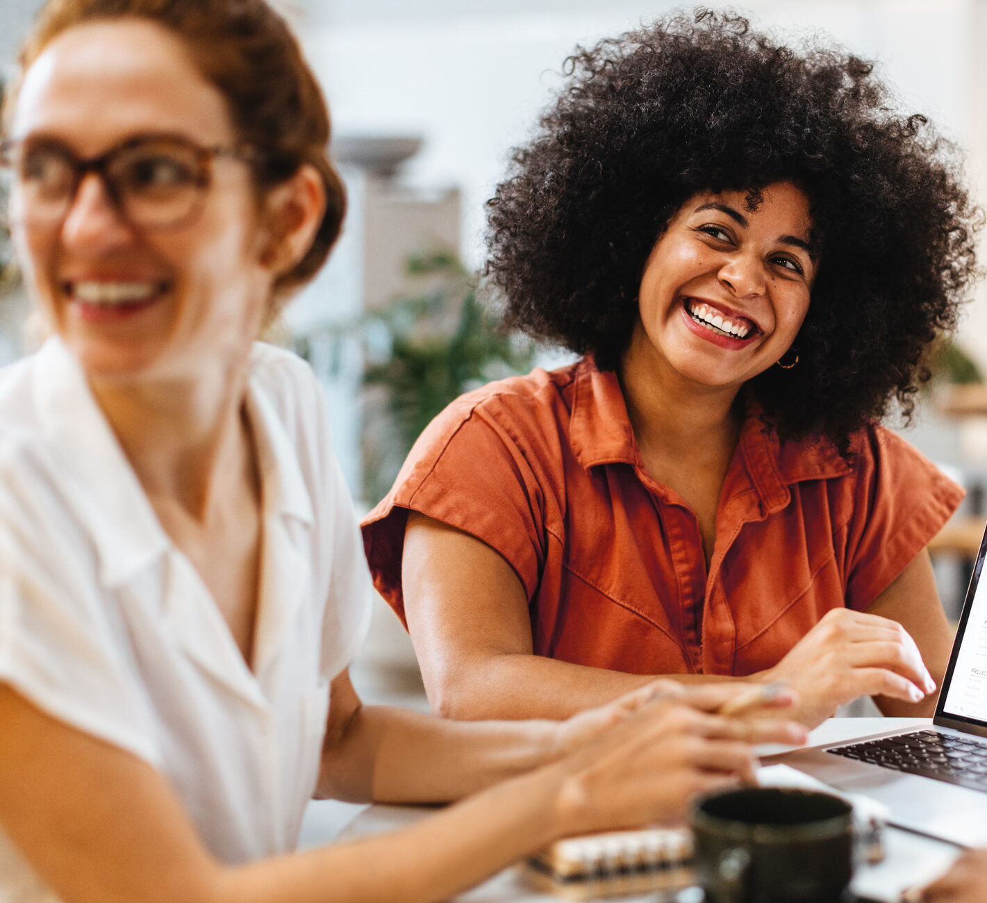 Group of happy remote professionals sitting in a cafe, engaged in a project and collaborating on ideas. Diverse business colleagues having a team meeting in a coffee shop.