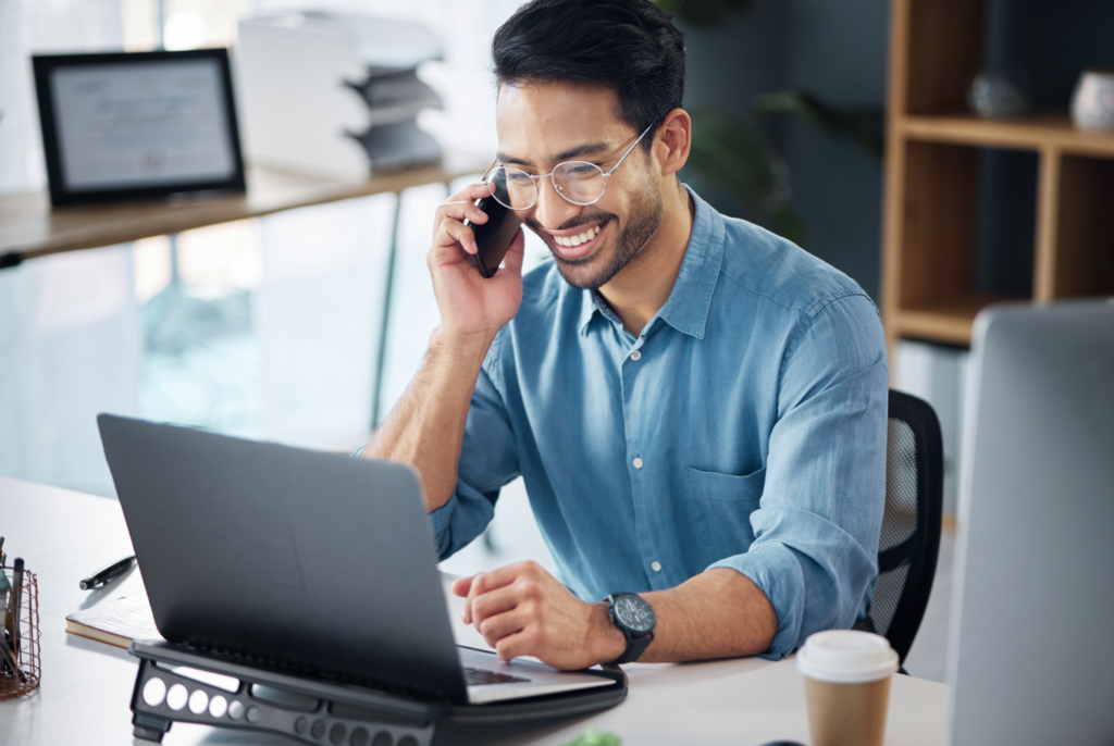 Man with coffee, on phone while working on laptop