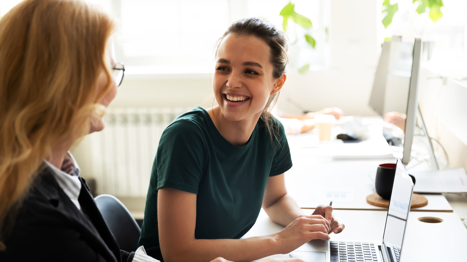 Two female corporate employees smiling and discussing work at computer