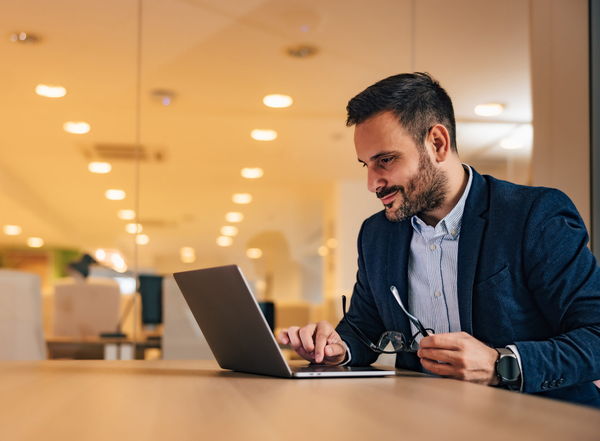 Successful businessman working over the laptop, reading something, surfing the web, sitting at the workplace.