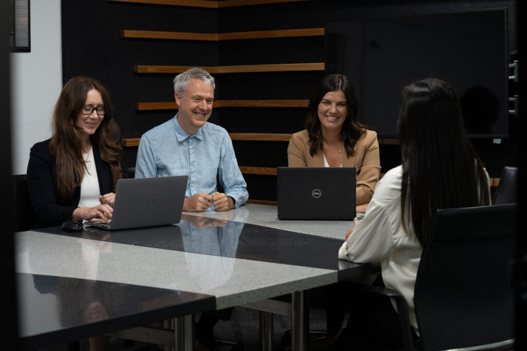 Three individuals seated at a table, each using a laptop, engaged in a collaborative work session.