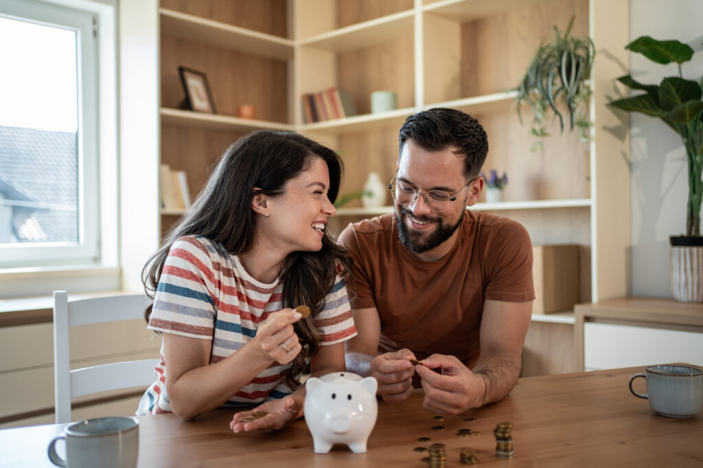 A woman and man, smiling are placing coins into a white piggy bank
